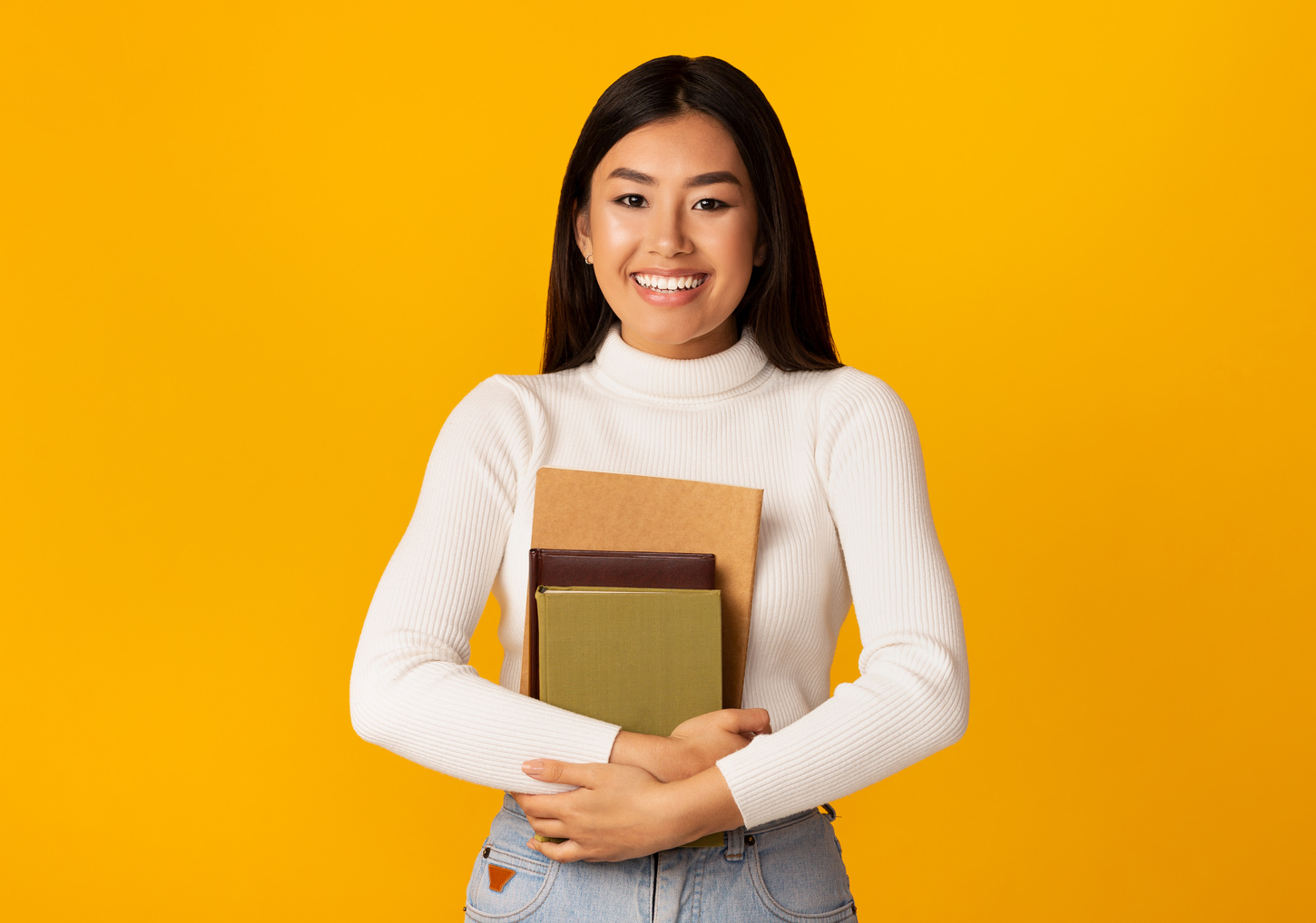 Students life. Student girl holding books, yellow background